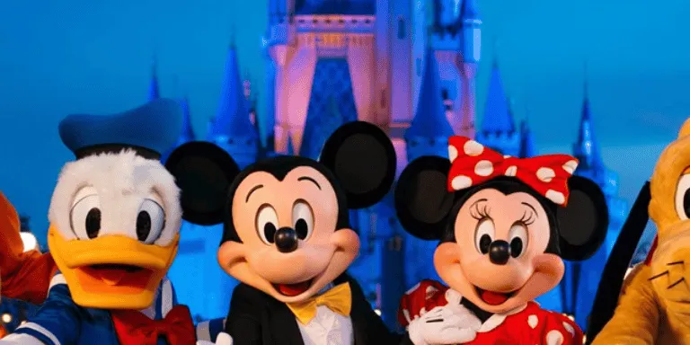 Goofy, Donald, Mickey, Minnie, and Pluto standing in front of Cinderella Castle at night