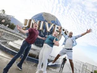 Three people jumping excitedly in front of the Universal Globe