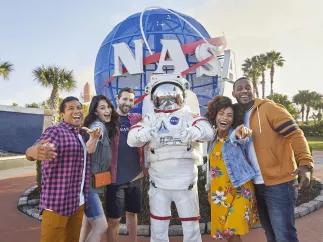 A group of 5 friends posing with someone in an space suit in front of the NASA logo
