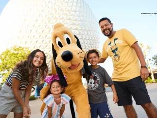 A mother and father with a young boy and young girl posing with Pluto in front of Spaceship Earth