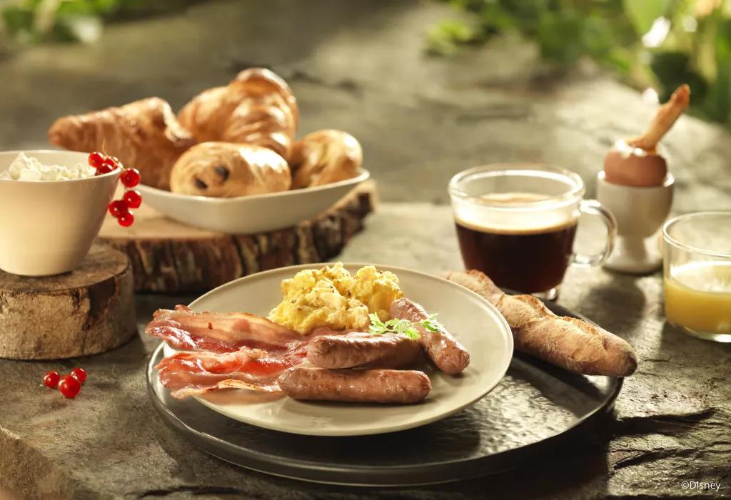 A plate of breakfast foods including sausages, bacon, eggs and croissants 