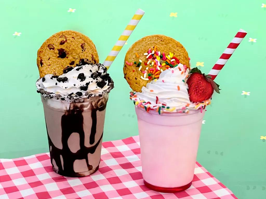 A chocolate and a strawberry milkshake, topped with whipped cream and cookies