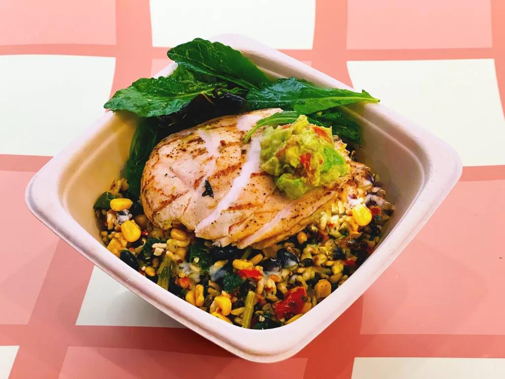 A bowl of mixed grains and vegetables topped with chicken and avocado