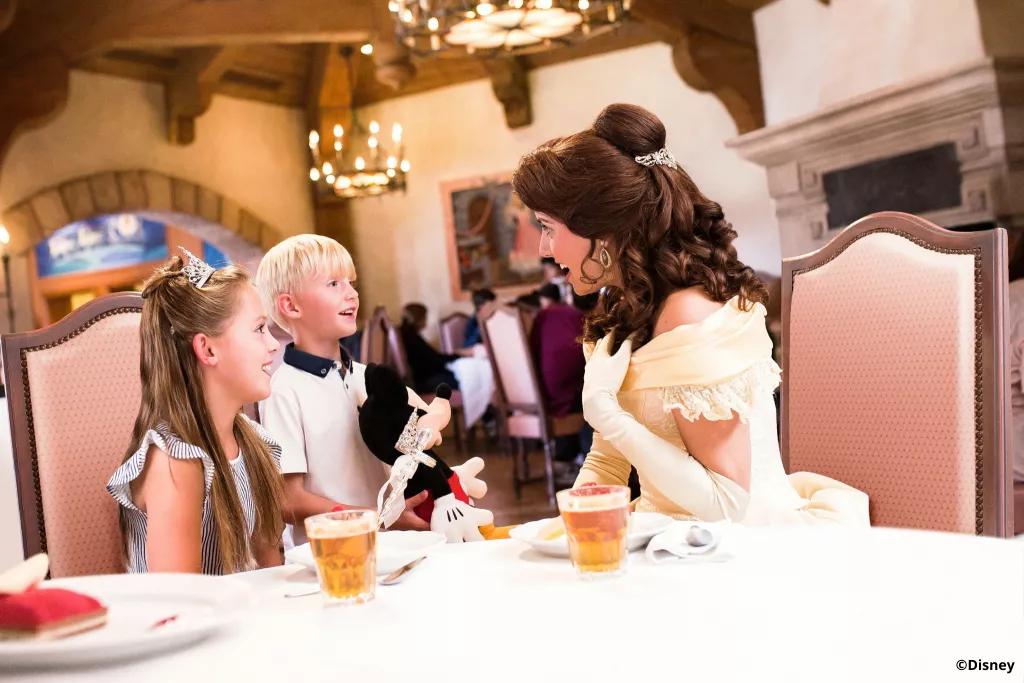 Belle speaking to two children dining at Auberge de Cendrillon