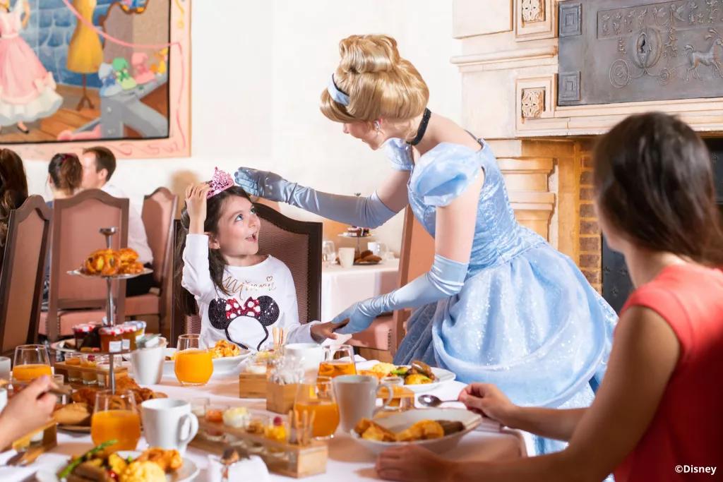 Cinderella talking to a young girl sat at a table at Auberge de Cendrillon