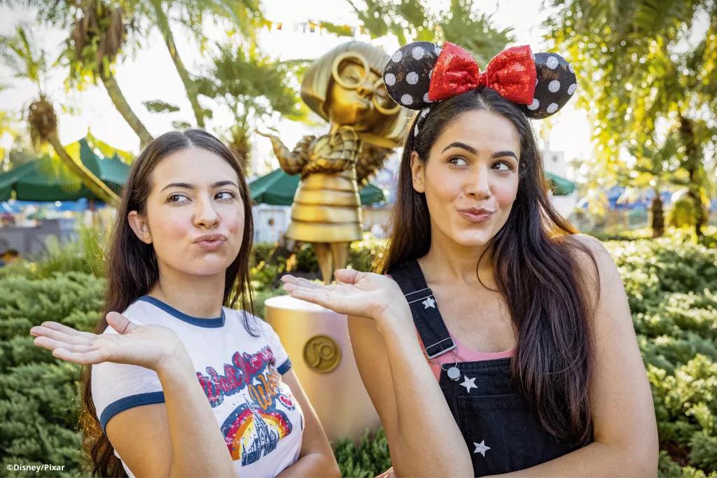 Two female guests posing with their hands raised in front of the Edna Mode golden statue