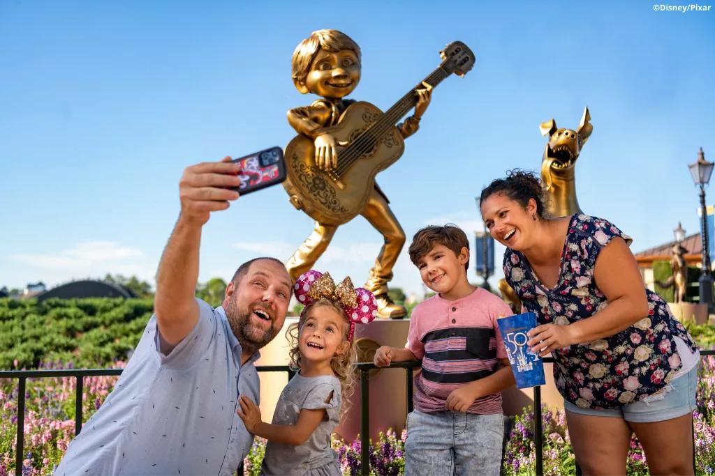 A family taking a selfie in front of the Miguel and Dante statues in EPCOT
