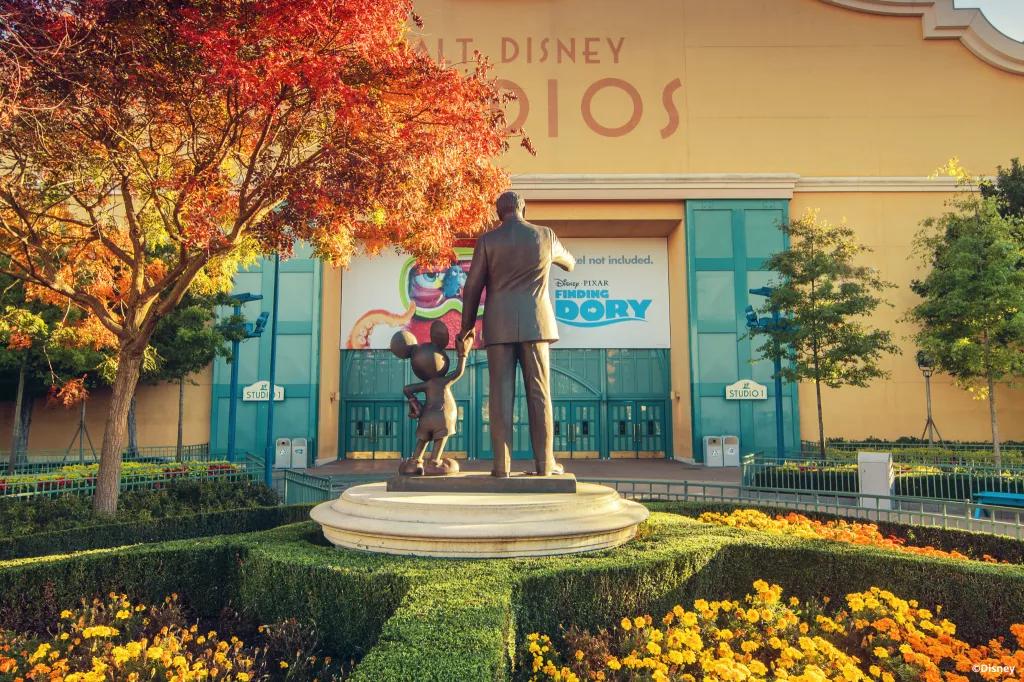 A statue of Mickey Mouse and Walt Disney facing away from the camera towards a sound stage