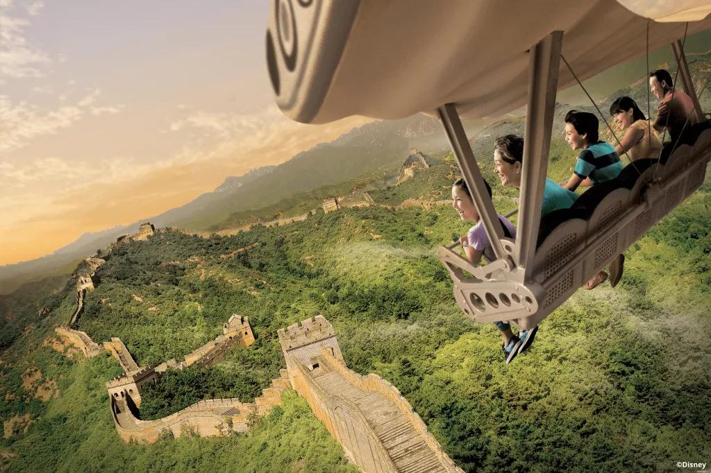 People in a ride vehicle flying over a simulation of the Great Wall of China