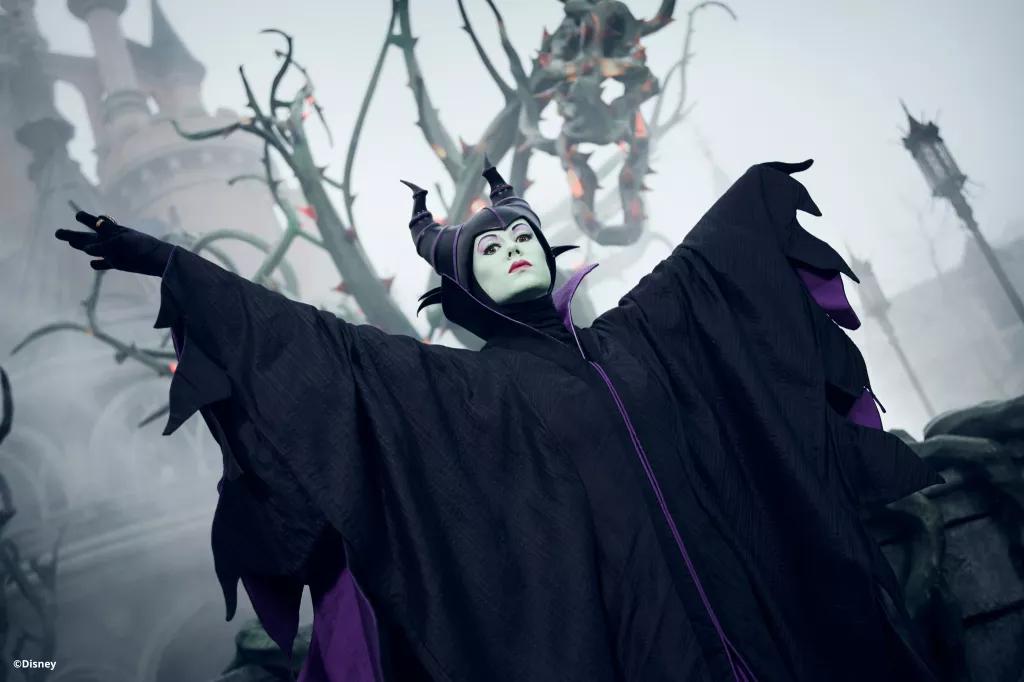 Maleficent standing with her arms outstretched in front of vines and fog