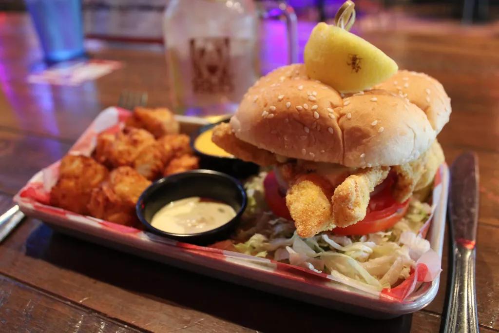A fried fish sandwich served with pickles and tater tots 