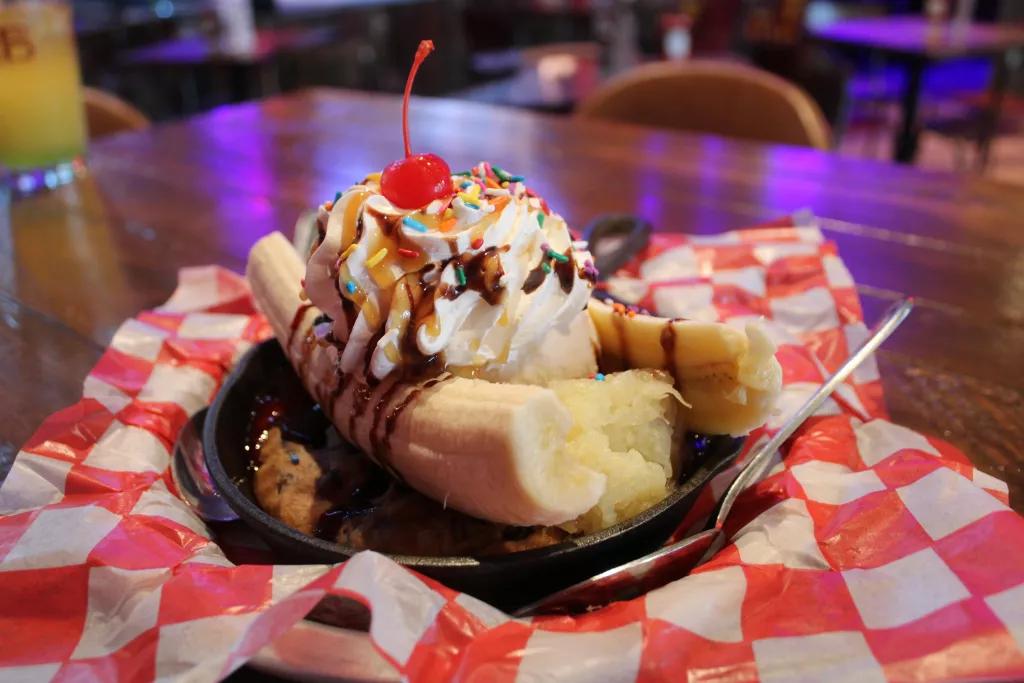 A banana split in a cookie skillet on top of a gingham cloth