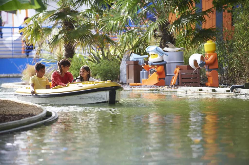 A woman and two children riding a LEGO boat along a winding waterway