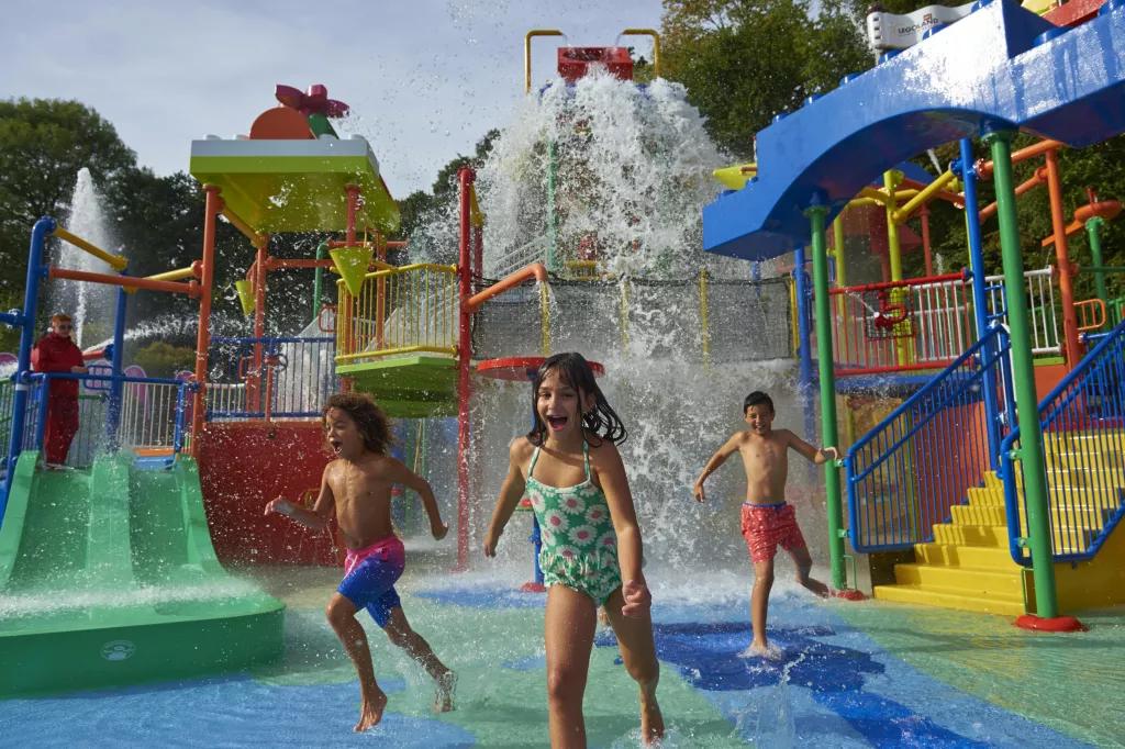 Three children in swimming costumes running away from a tipping bucket of water