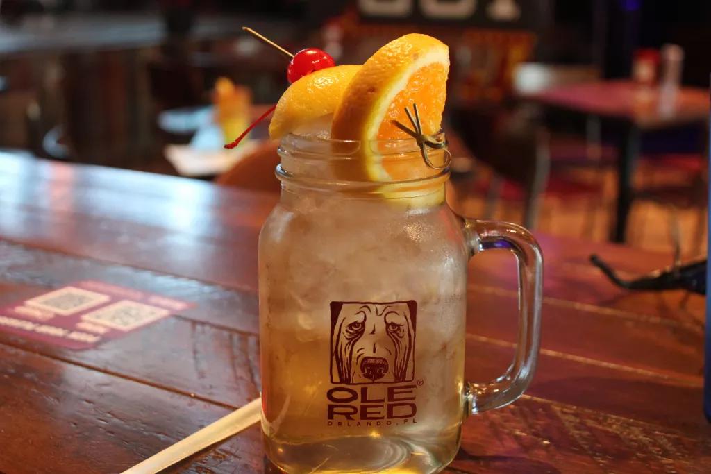 A mason jar glass of white sangria on a wooden bar topped with orange slices