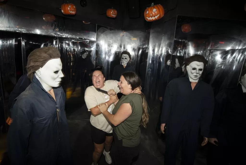 Two women surrounded by multiple scare actors dressed as Michael Myers from Halloween