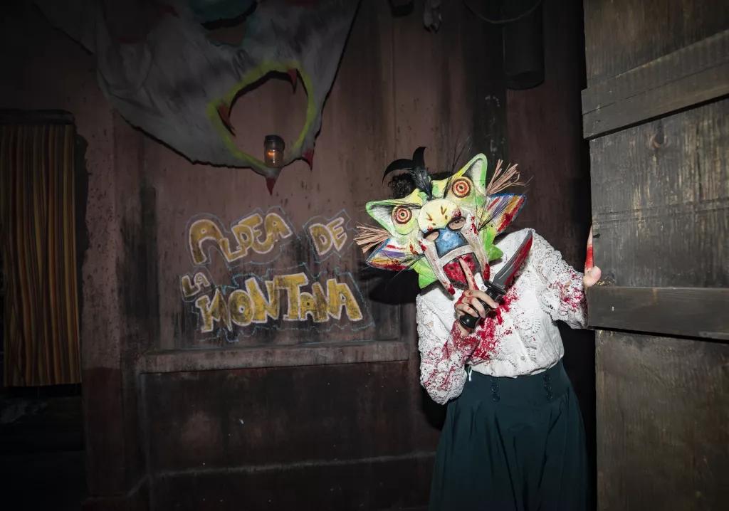A scare actors wearing a mask and holding a knife covered in blood looking at the camera
