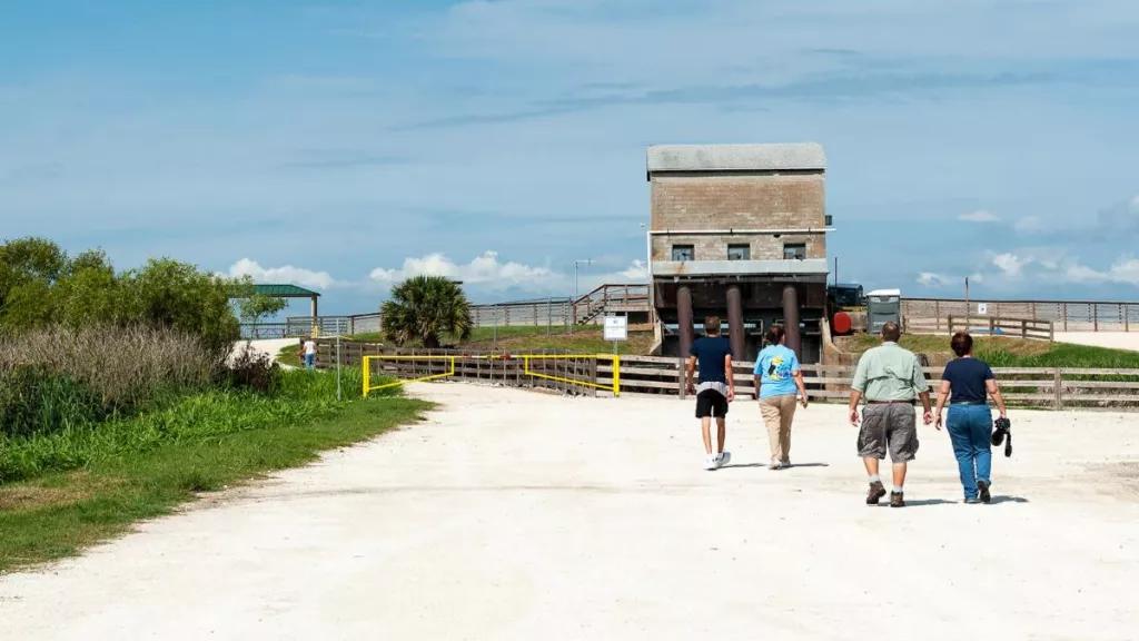 4 adults walking along a sandy road towards a hut and the water of Lake Apopka