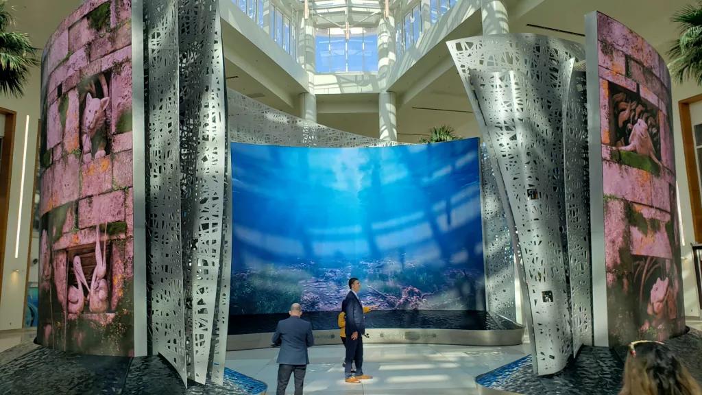 Two men standing within three large curved screens showing videos of underwater 