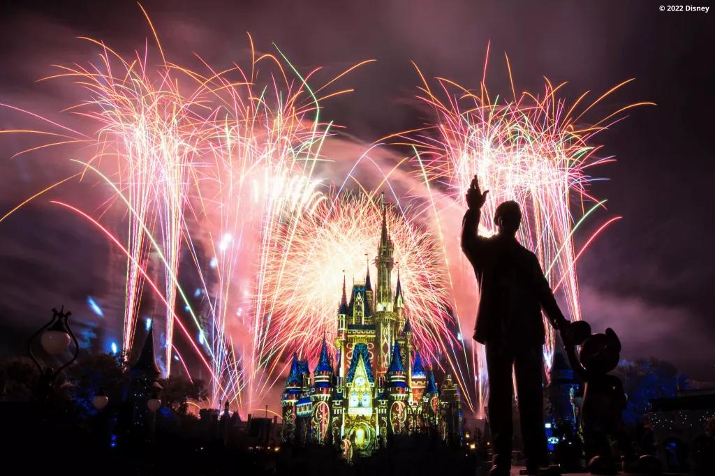 Cinderella Castle lit up with fireworks in the background and a statue of Mickey and Walt in the foreground