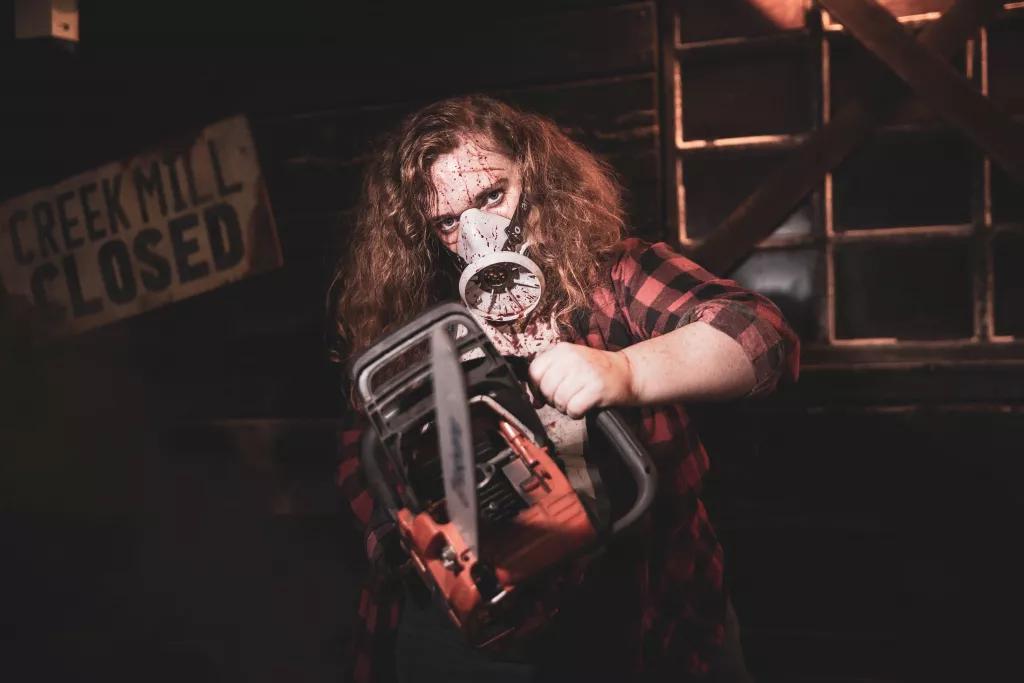 A man in a checked shirt and wearing a gas mask splattered with blood and holding a chainsaw