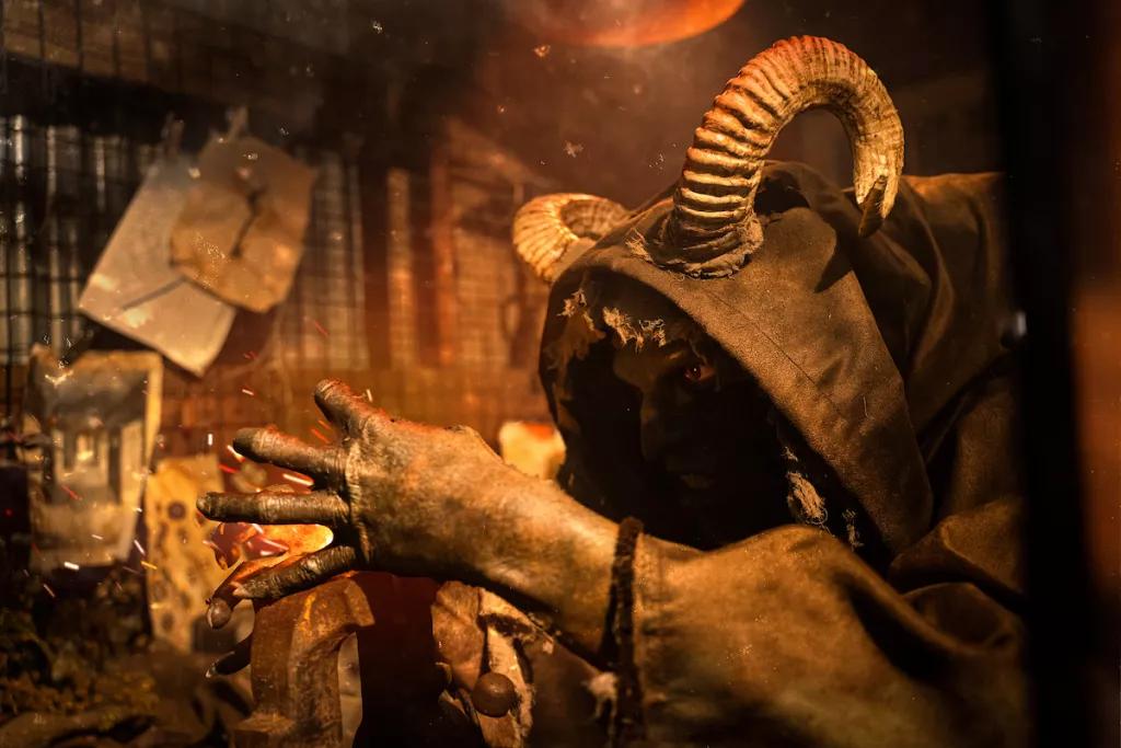 A creature with curved horns and a hooded cloak leaning over a blacksmith's block