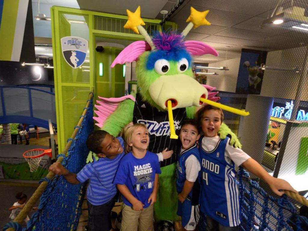 Four young children in Orlando Magic tshirts posing with a green dragon mascot