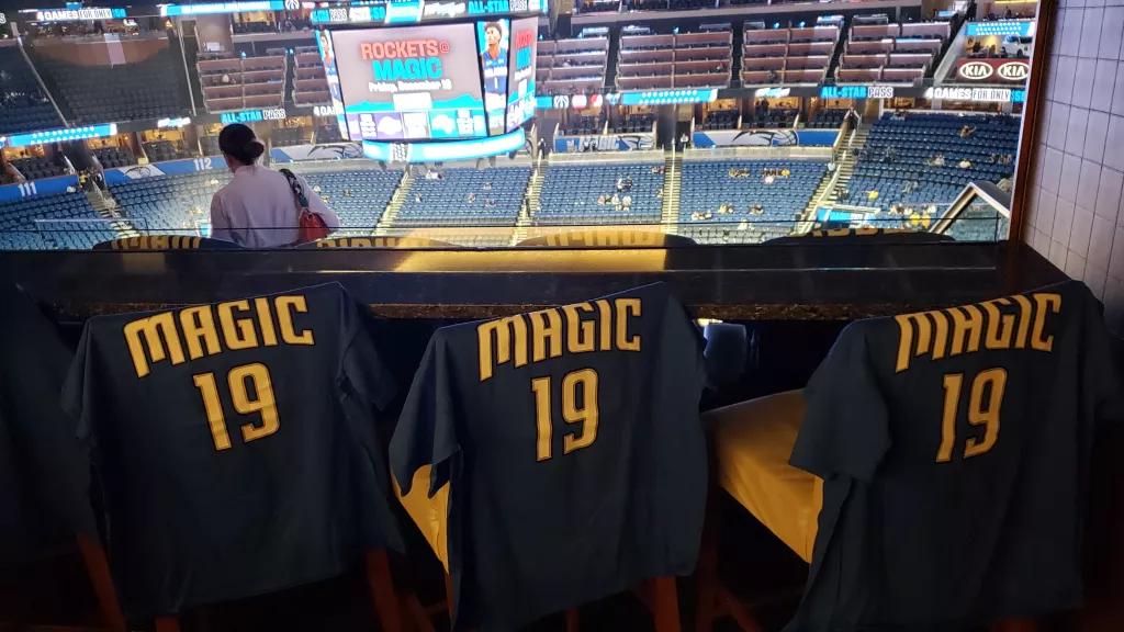 3 Orlando Magic tops hung on the back of bar stools with a view of the basketball court