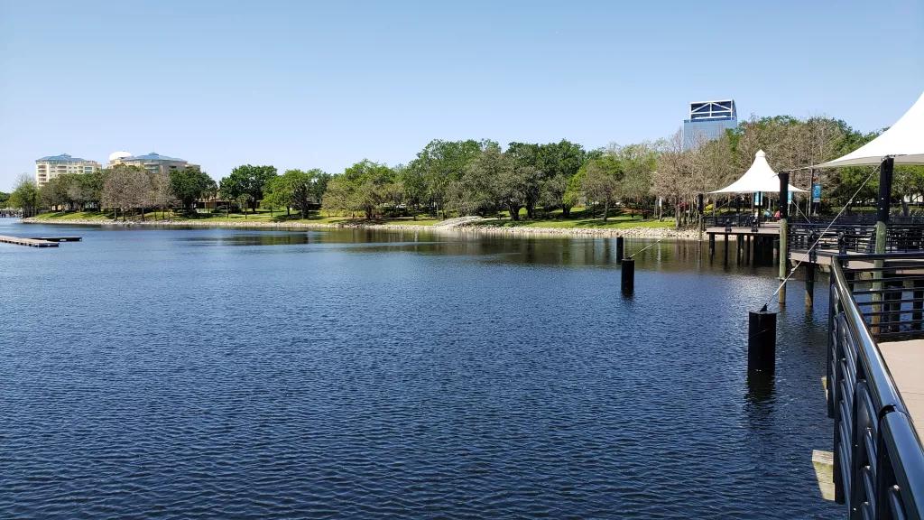 A calm lake in front of a grassy bank lined with trees and a clear blue sky