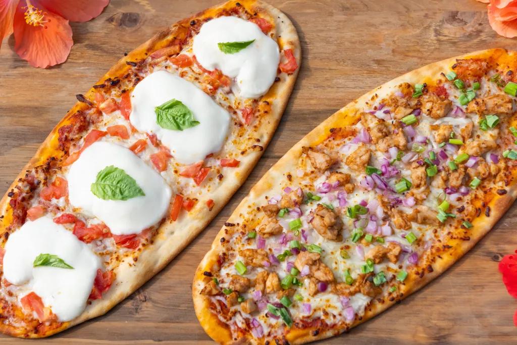 Two thin crust pizzas on a wooden board surrounded by flowers