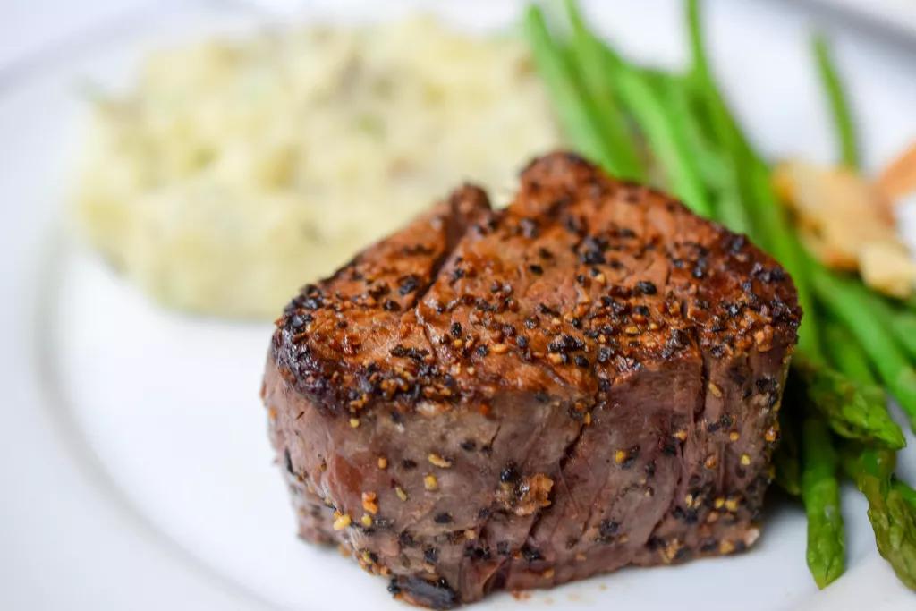 A cooked filet steak on a plate with mashed potatoes and green beans