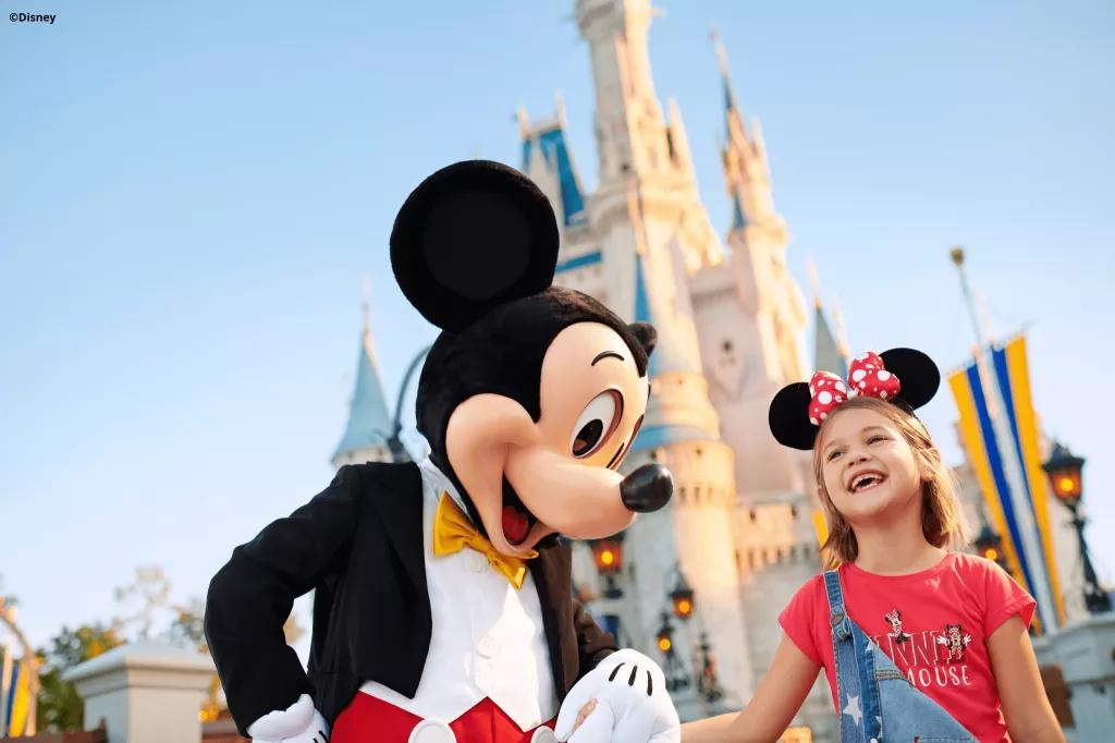 Mickey Mouse holding hands with a young girl in front of Cinderella Castle 