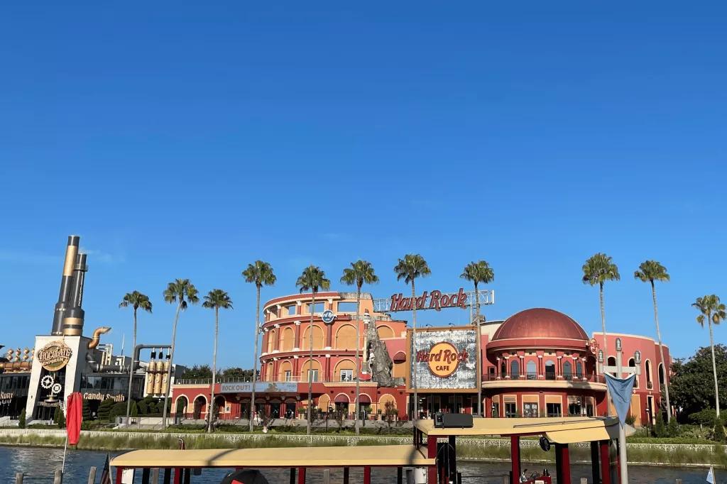 The exterior of the Hard Rock Cafe seen across a waterway, behind a row of palm trees