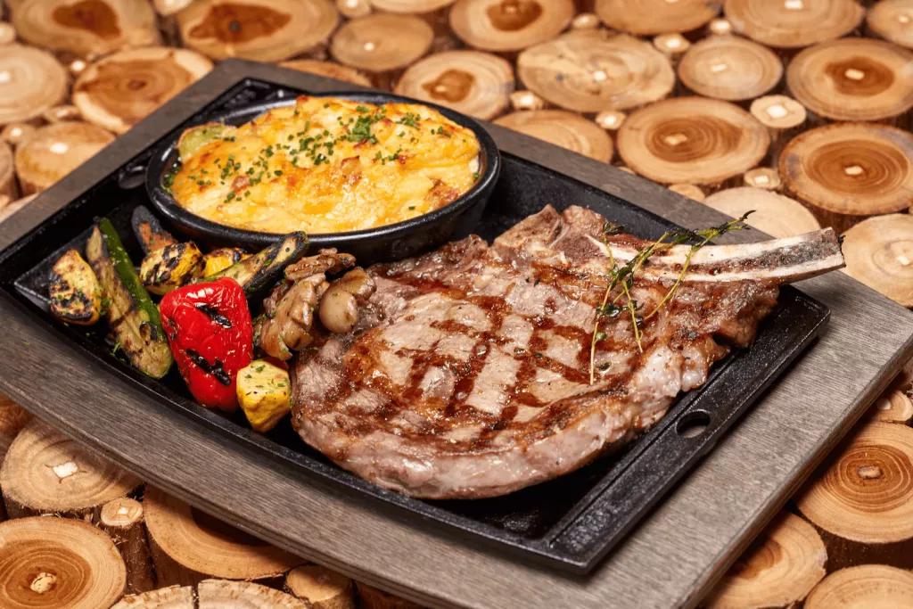 A ribeye steak with mac and cheese and roasted vegetables on a metal tray