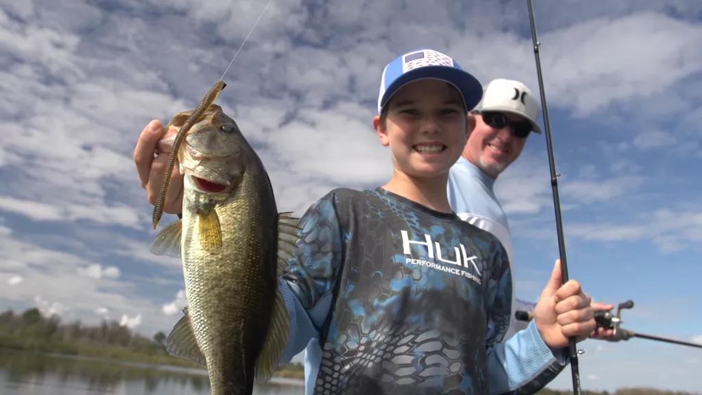 A boy holding a fishing rod in one hand and a bass in the other