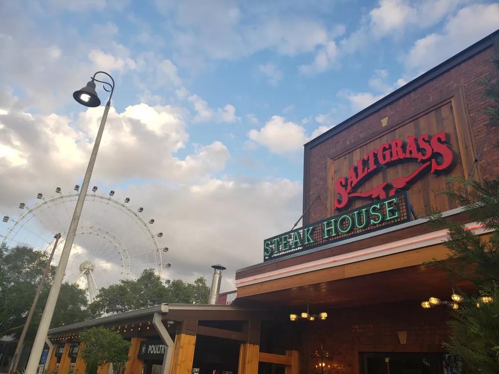 The outside of Saltgrass Steakhouse clad with wood panels, with The Wheel in the background