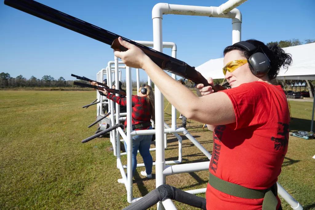 A woman in a red tshirt at the front of a line of people pointing guns for clay pigeon shooting