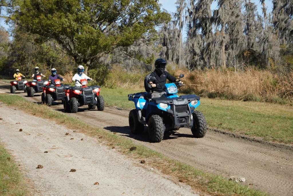 Four people on quad bikes following an instructor in a line along a dirt path surrounded by trees