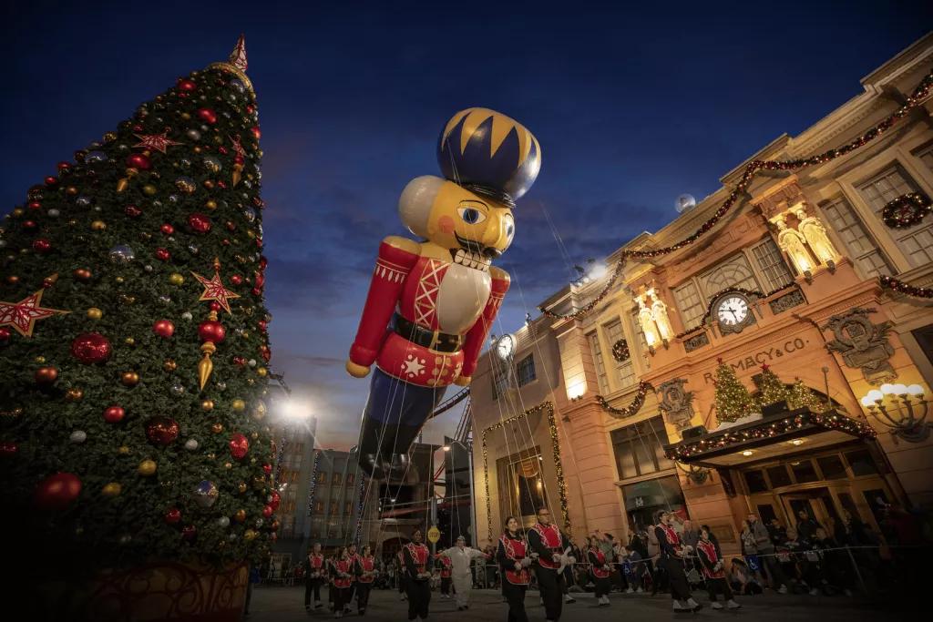 A large balloon shaped like a nutcracker being carried on string, passing next to a large Christmas tree