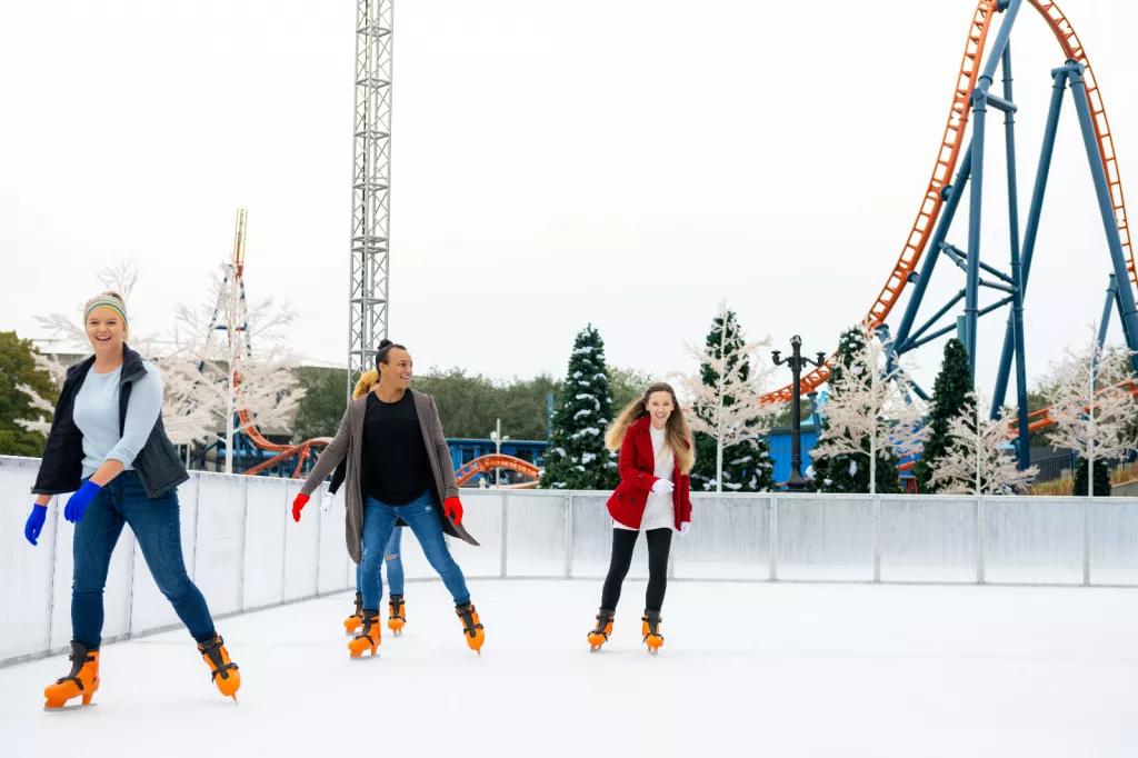 4 adults ice skating outdoors in front of a rollercoaster