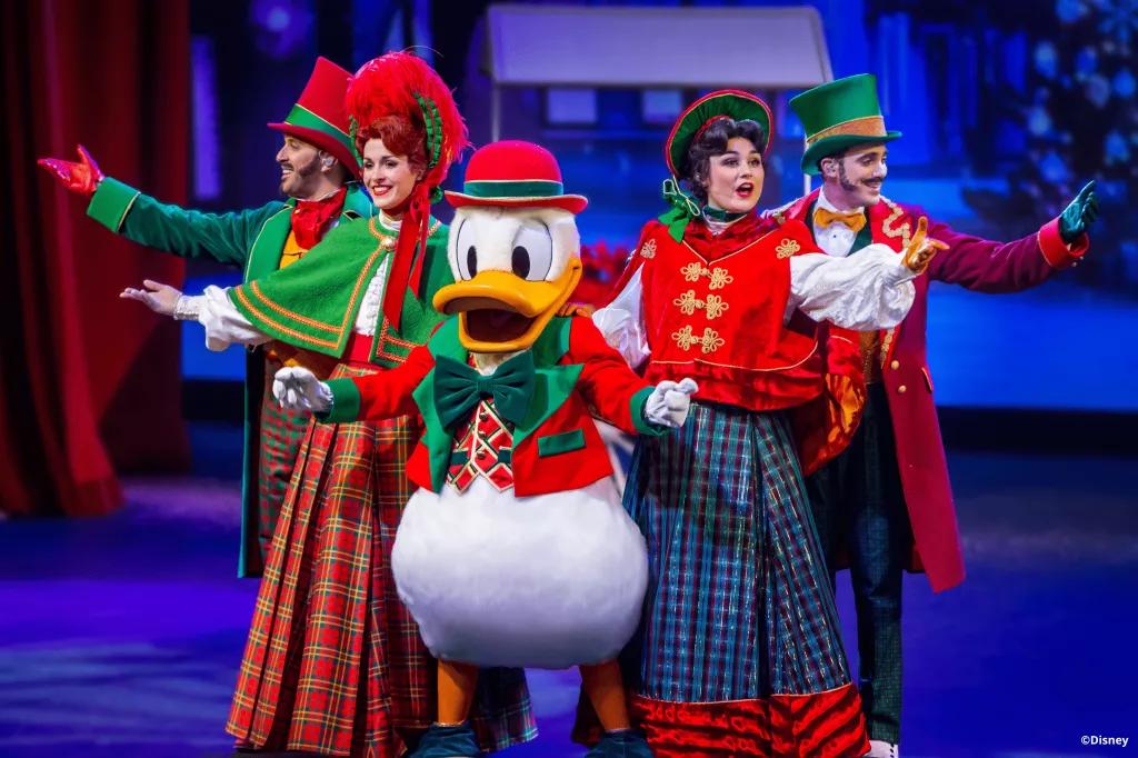 Donald Duck standing with four carol singers, all wearing Victorian style Christmas outfits