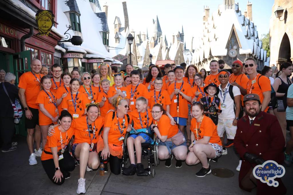 A large group of children and adults wearing bright orange tshirts standing in the Wizarding World of Harry Potter