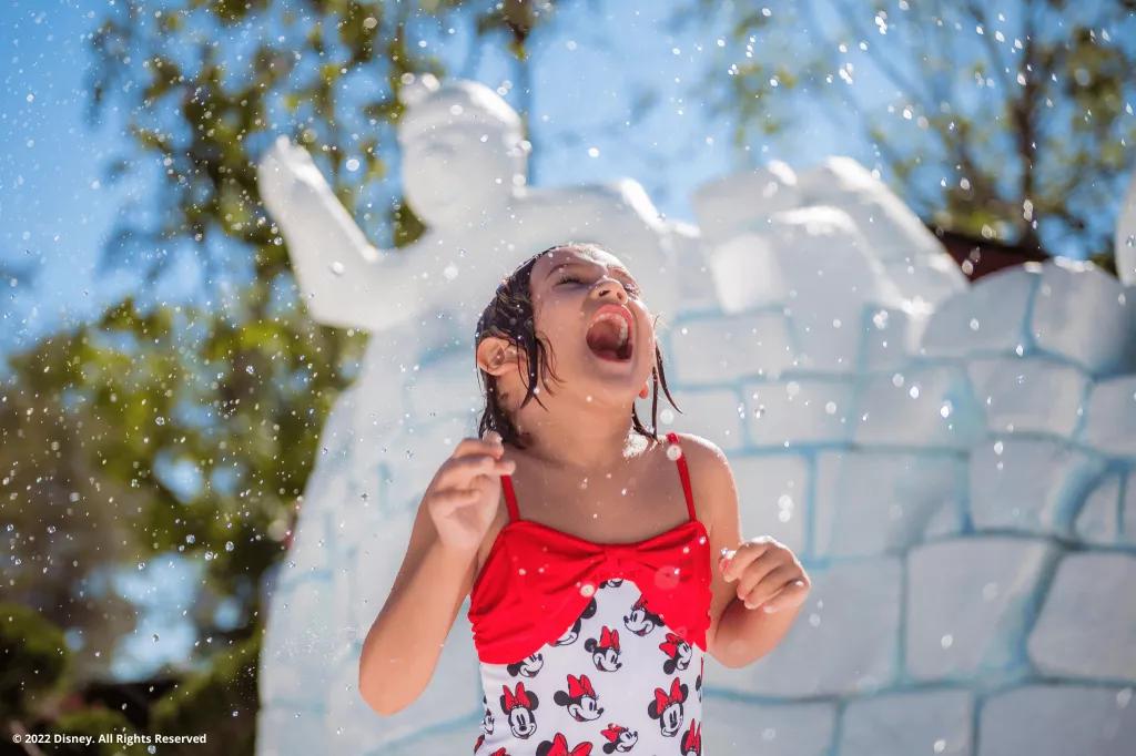 A small girl in a Minnie Mouse swimming costume in front of a fake igloo in a water park