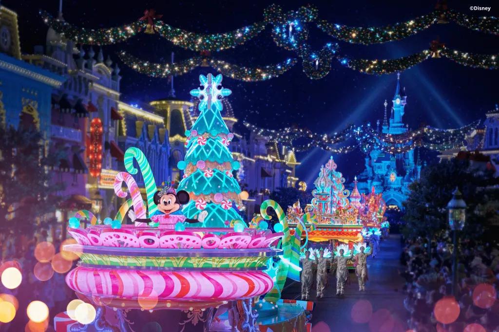 Christmas parade floats lit up with neon lights carrying Disney characters including Minnie Mouse. Sleeping Beauty Castle is in the background