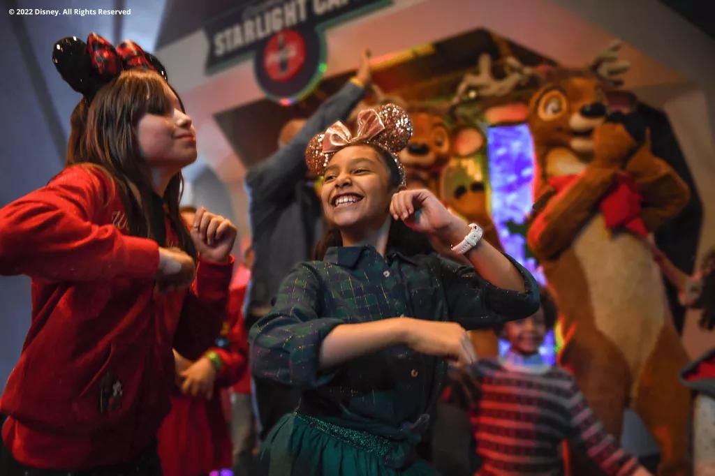 Two young girls wearing Minnie ears dancing with two reindeer in the background