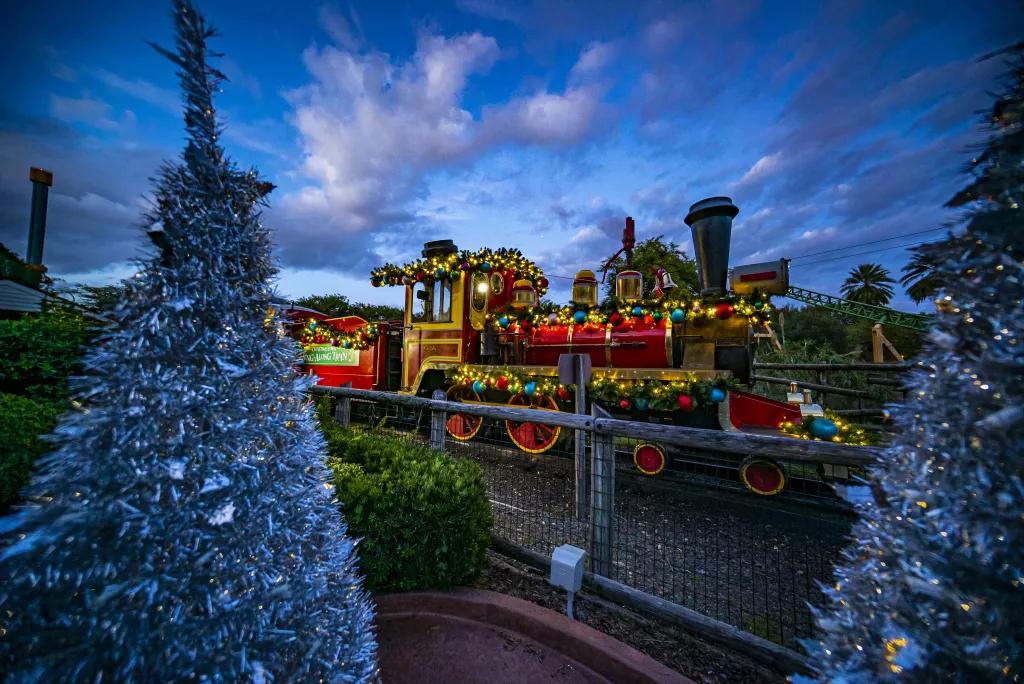 A train decorated with colourful tinsel on a track next to some silver Christmas trees