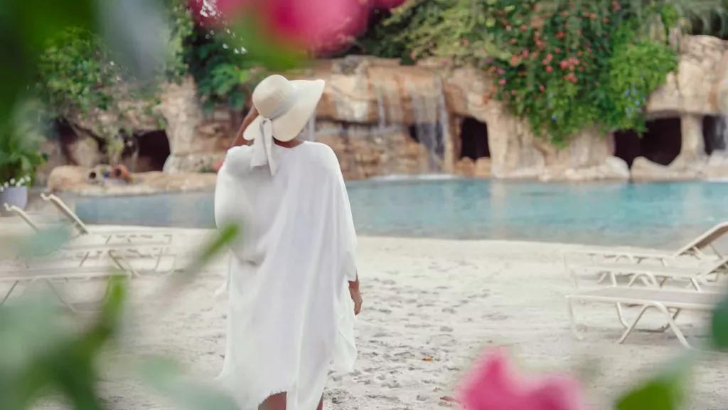 A woman in a straw hat and beach cover-up walking along an empty beach