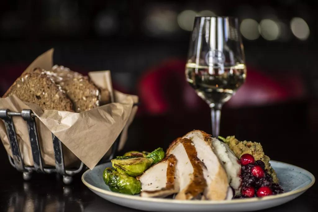 A plate of sliced turkey, stuffing and cranberry sauce, next to a glass of wine and a basket of bread