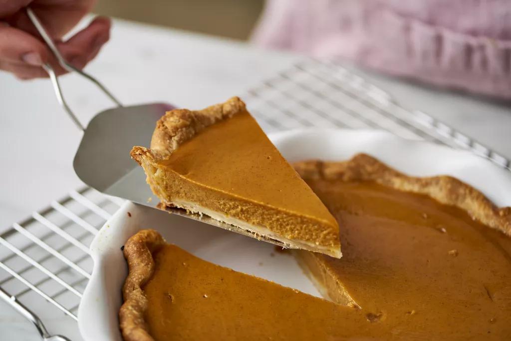 A slice of pumpkin pie being lifted out of a pie tin