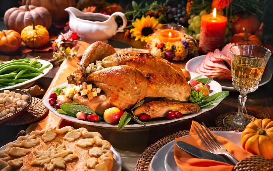 A table full of Thanksgiving food including turkey, ham and pumpkin pie, and decorated with pumpkins